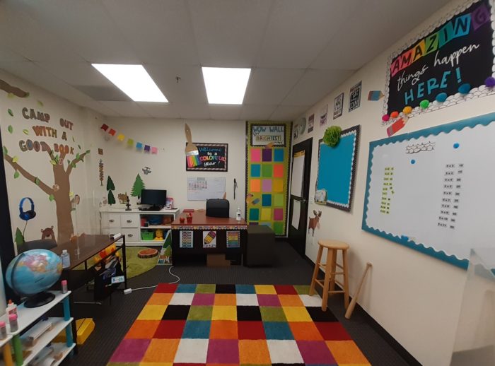 small classroom with colorful carpet and walls covered with assignments