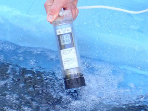 A hand holding a pme miniDOT data logger in the water.